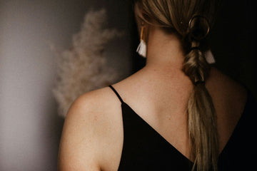 A woman using a hair straightener on her long, sleek hair in a home setting, with hair curlers and styling products on a nearby vanity table.